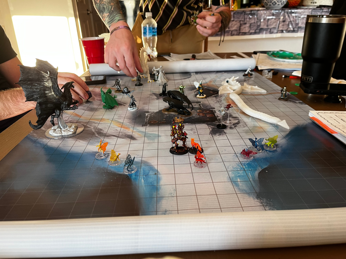 DnD game in progress with figurines on a grid map, players' hands reaching to move pieces.