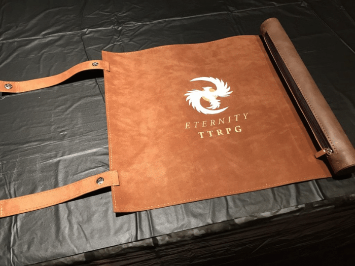 Brown leather RPG game mat with a rolled-up tube and straps, imprinted with the logo 
