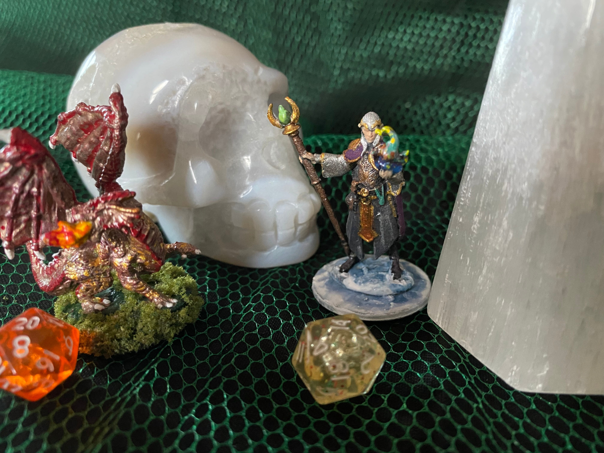 Miniatures and dice arranged on green mesh with a skull and crystal.