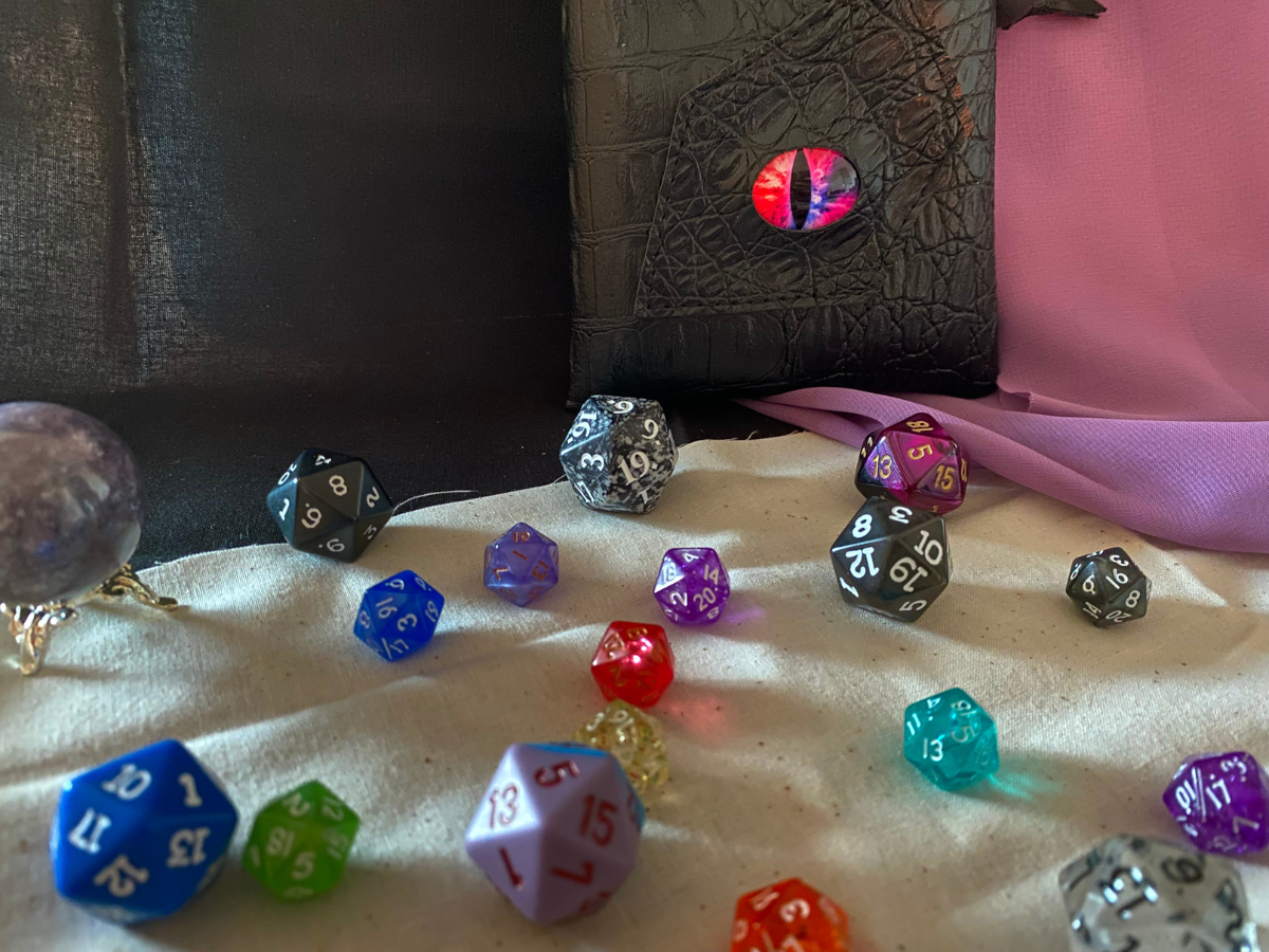 Assorted dice scattered on a white cloth with a crystal ball and a book adorned with a glowing eye.