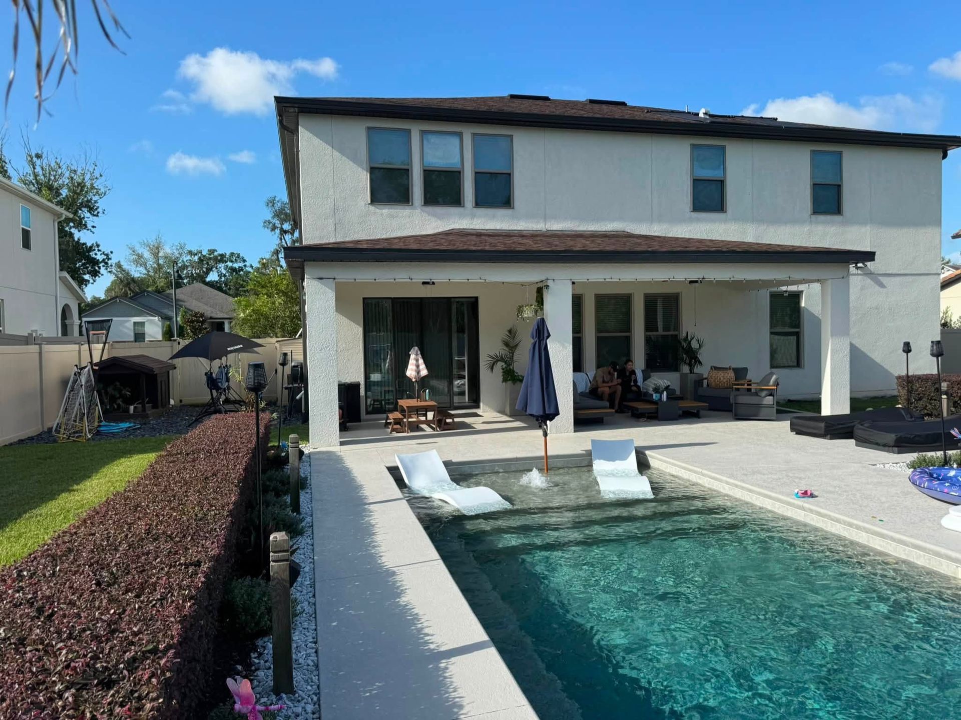 Backyard with a two-story house and covered patio beside a turquoise swimming pool under a blue sky