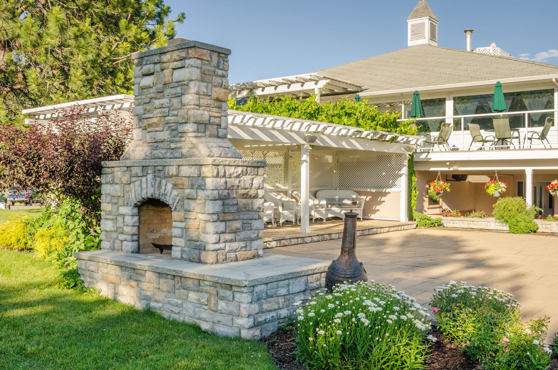Stone outdoor fireplace with a white pergola and building in the background on a sunny day. Stone outdoor fireplace with a white pergola and building in the background on a sunny day.