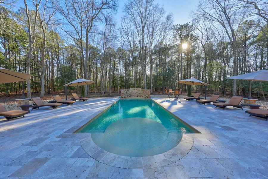 Swimming pool with lounge chairs and umbrellas in a forest setting.