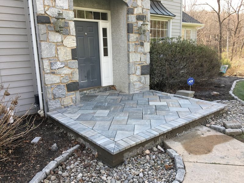 Gray stone entryway with a dark gray door and a patterned paver patio.