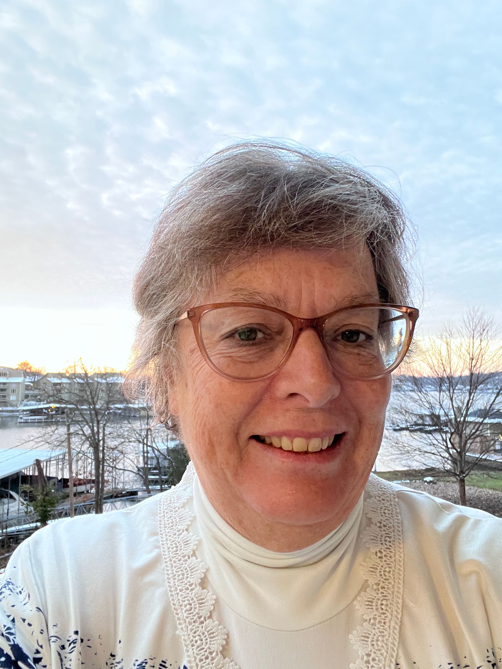 Woman with glasses smiles outdoors, with a mountain backdrop.