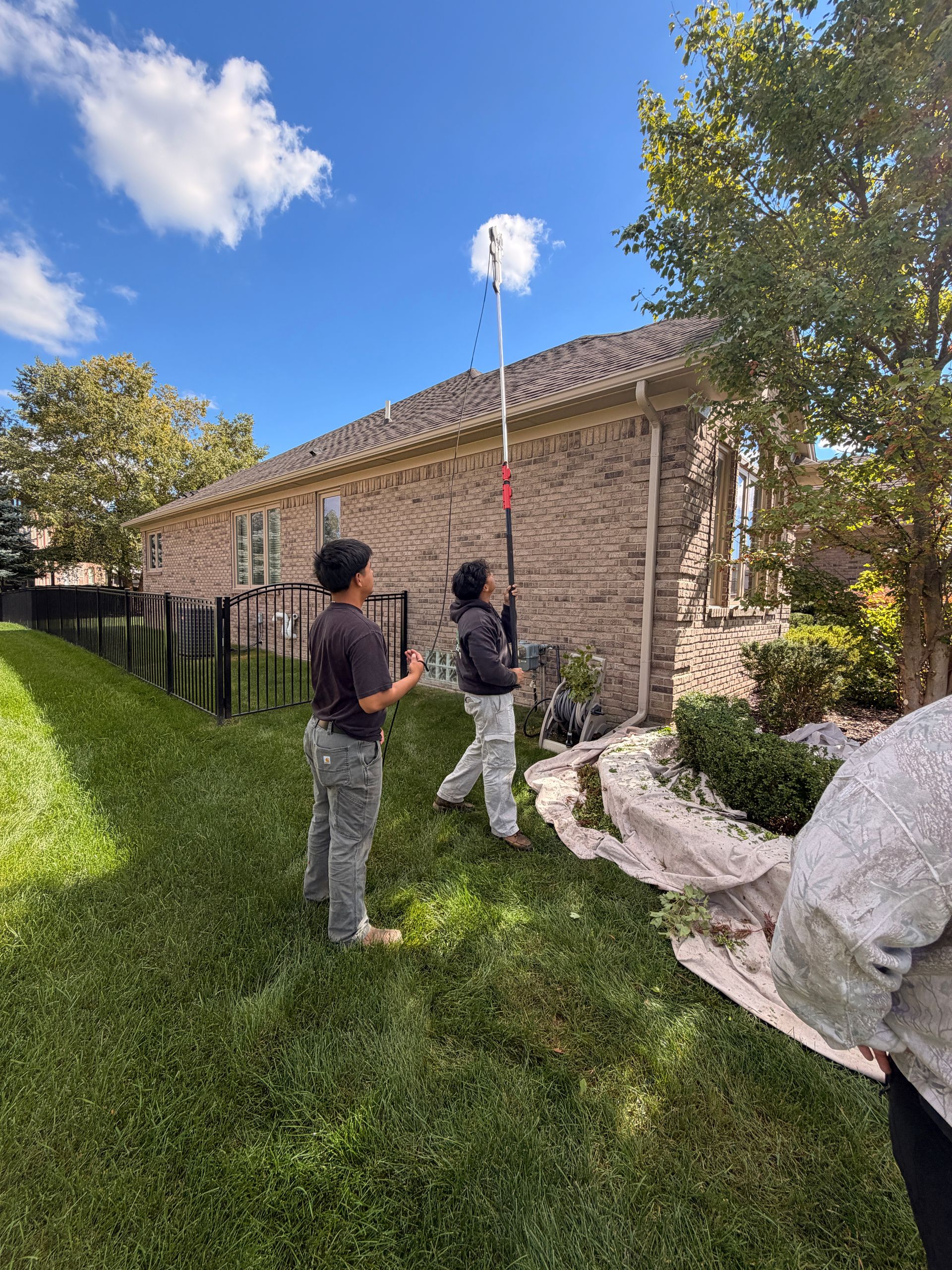 Two people raising a measuring pole beside a stone building on a sunny grassy lawn