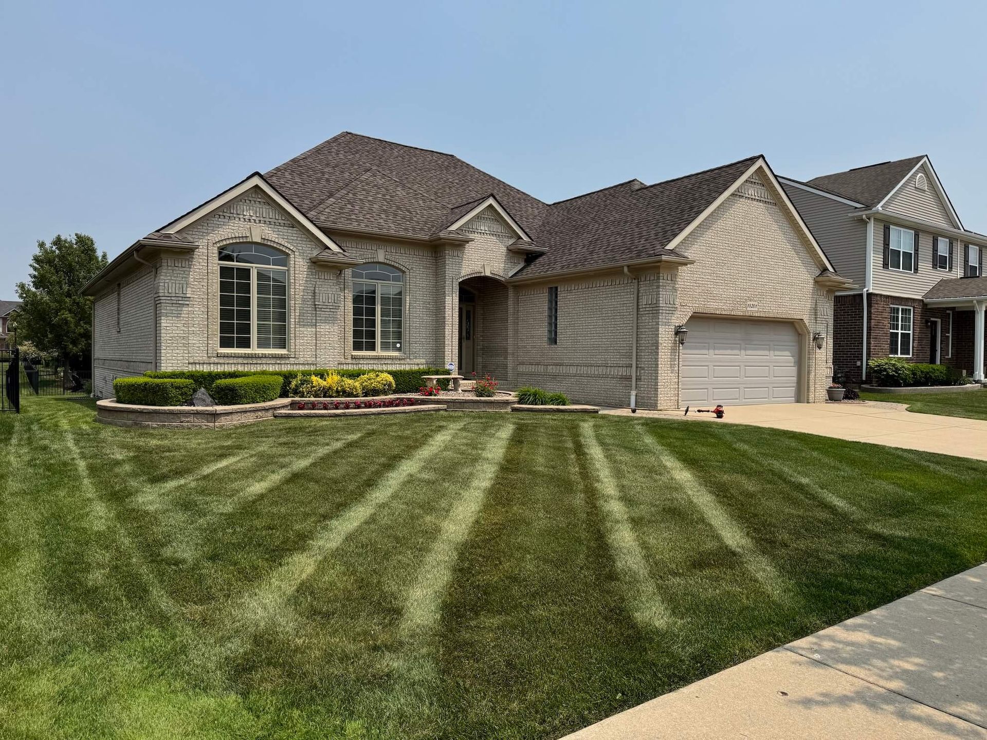 A brick house with a lawn mowed in straight lines. A neighbor's house is visible on the right.