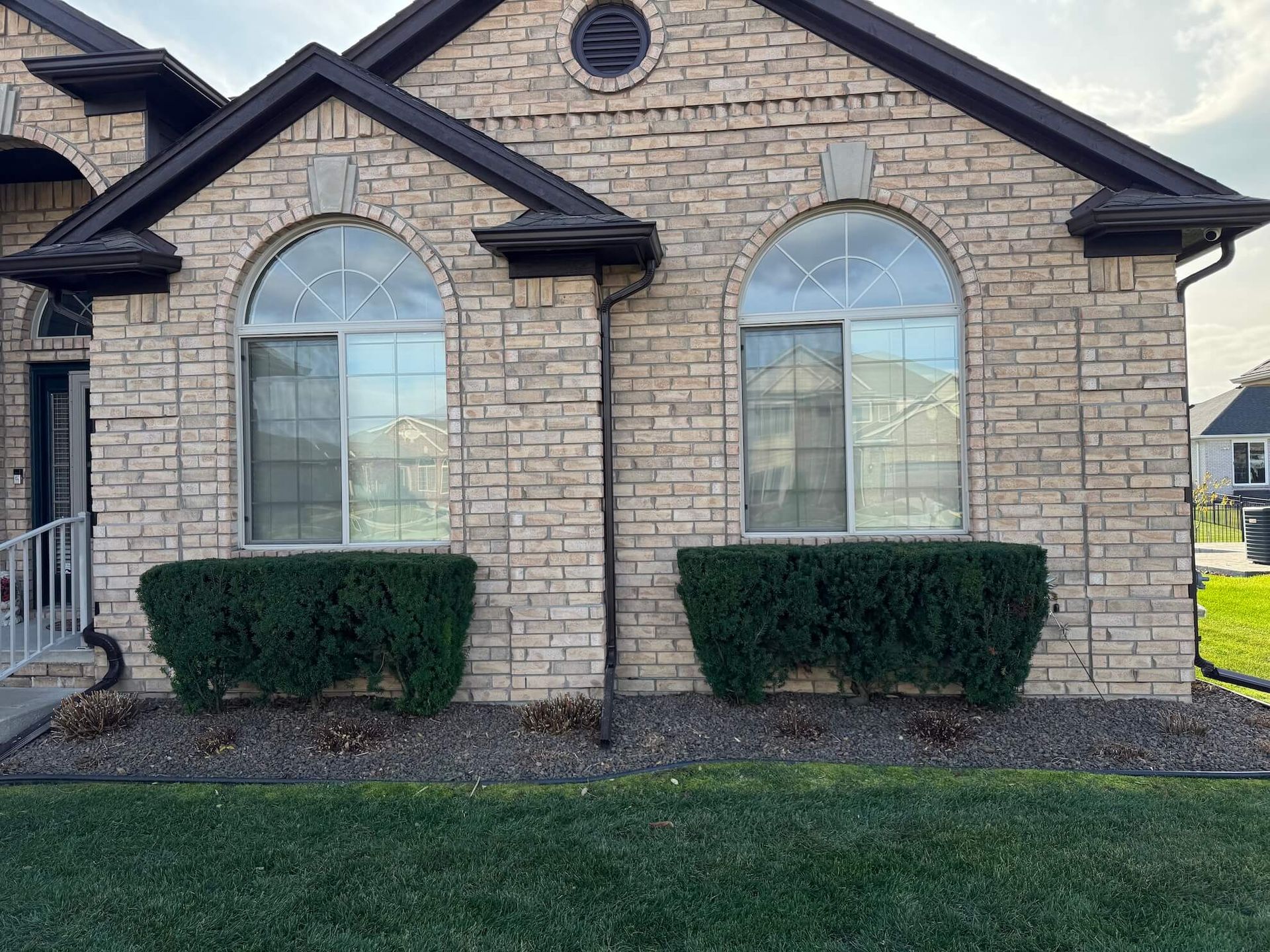 Stone brick house with arched windows, dark trim, and green bushes along the foundation.