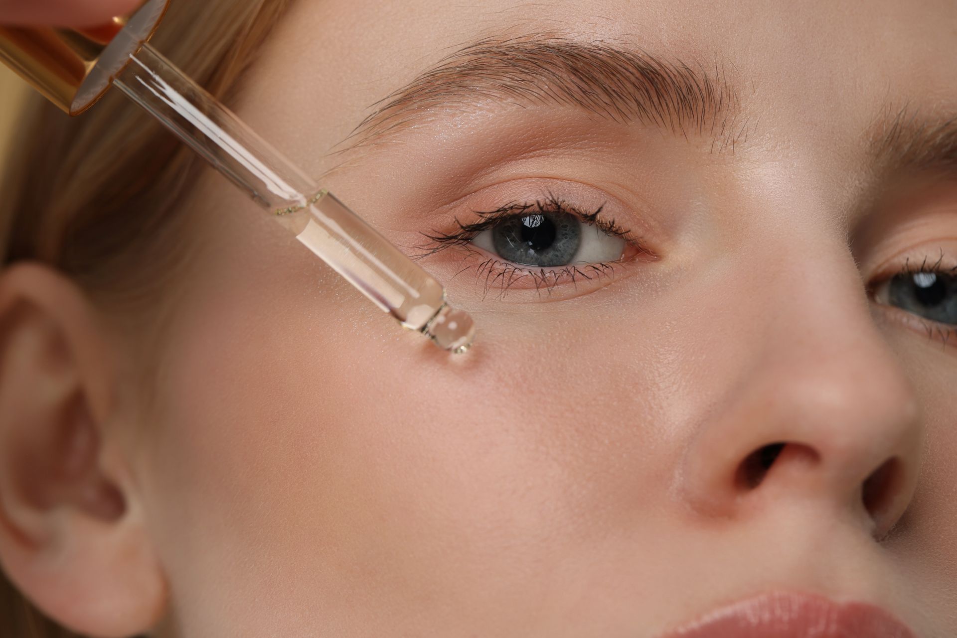 A woman is applying a serum to her face with a pipette.
