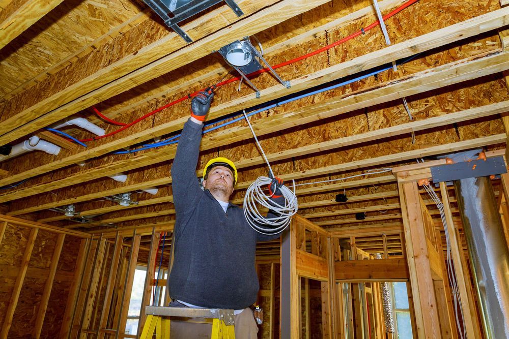 An electrician is working on the ceiling of a house under construction.