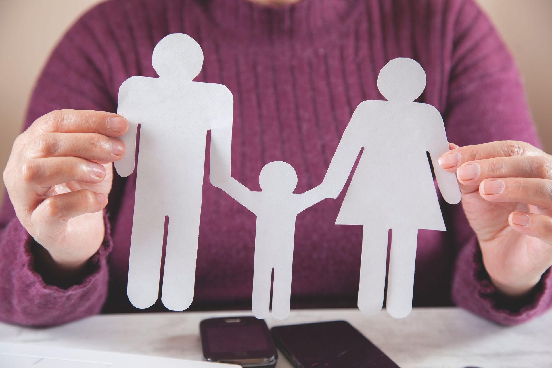 Hands holding white paper cutouts of a family in front of a purple sweater background
