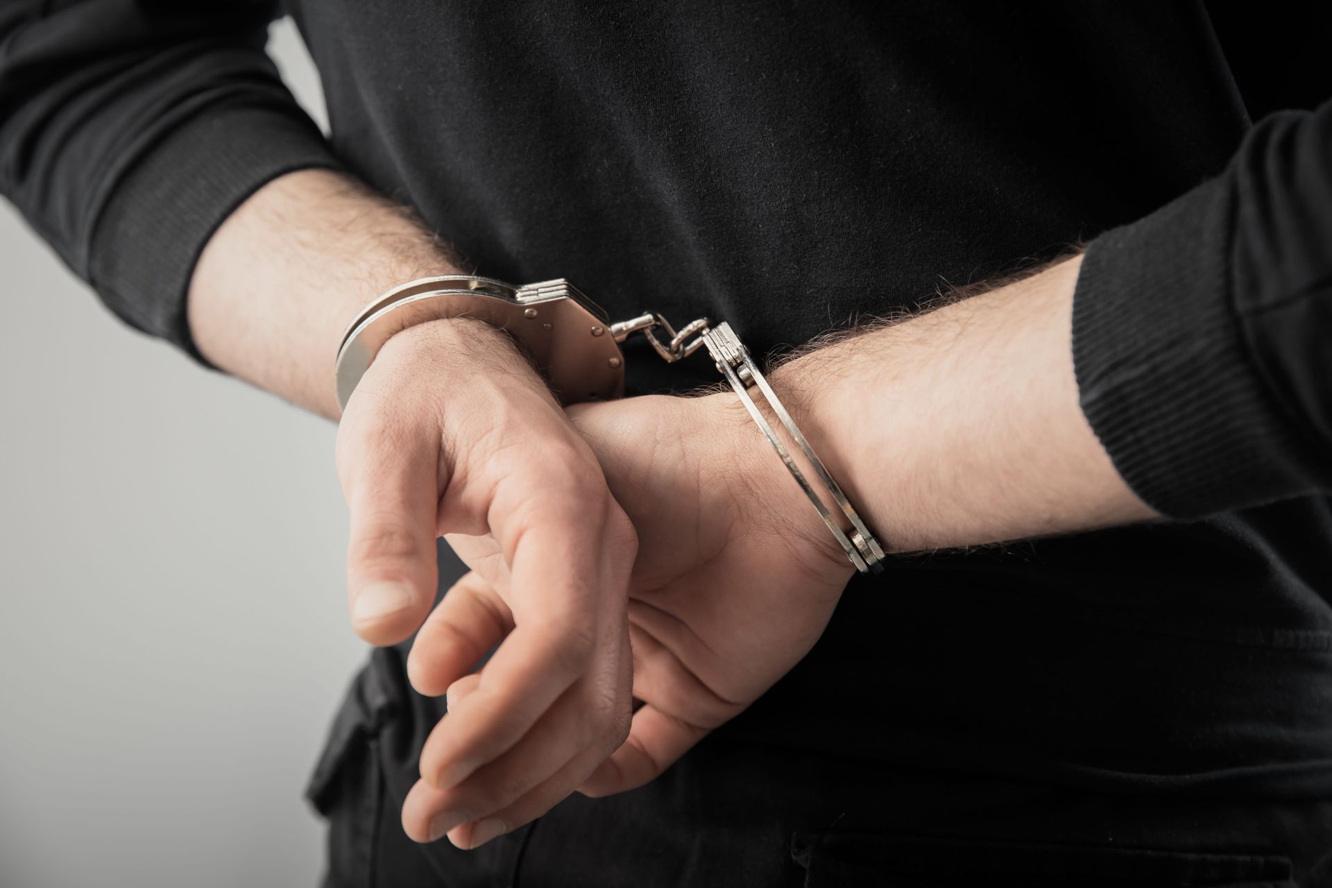 Handcuffed hands in a black long-sleeve shirt against a gray background