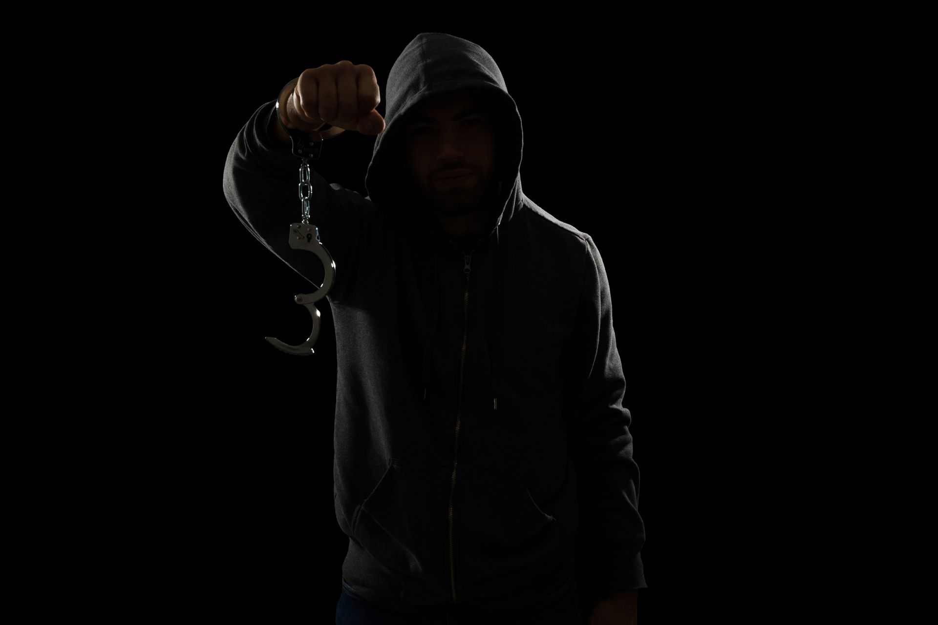 Shadowy hooded figure holding up a metal chain in a dark setting