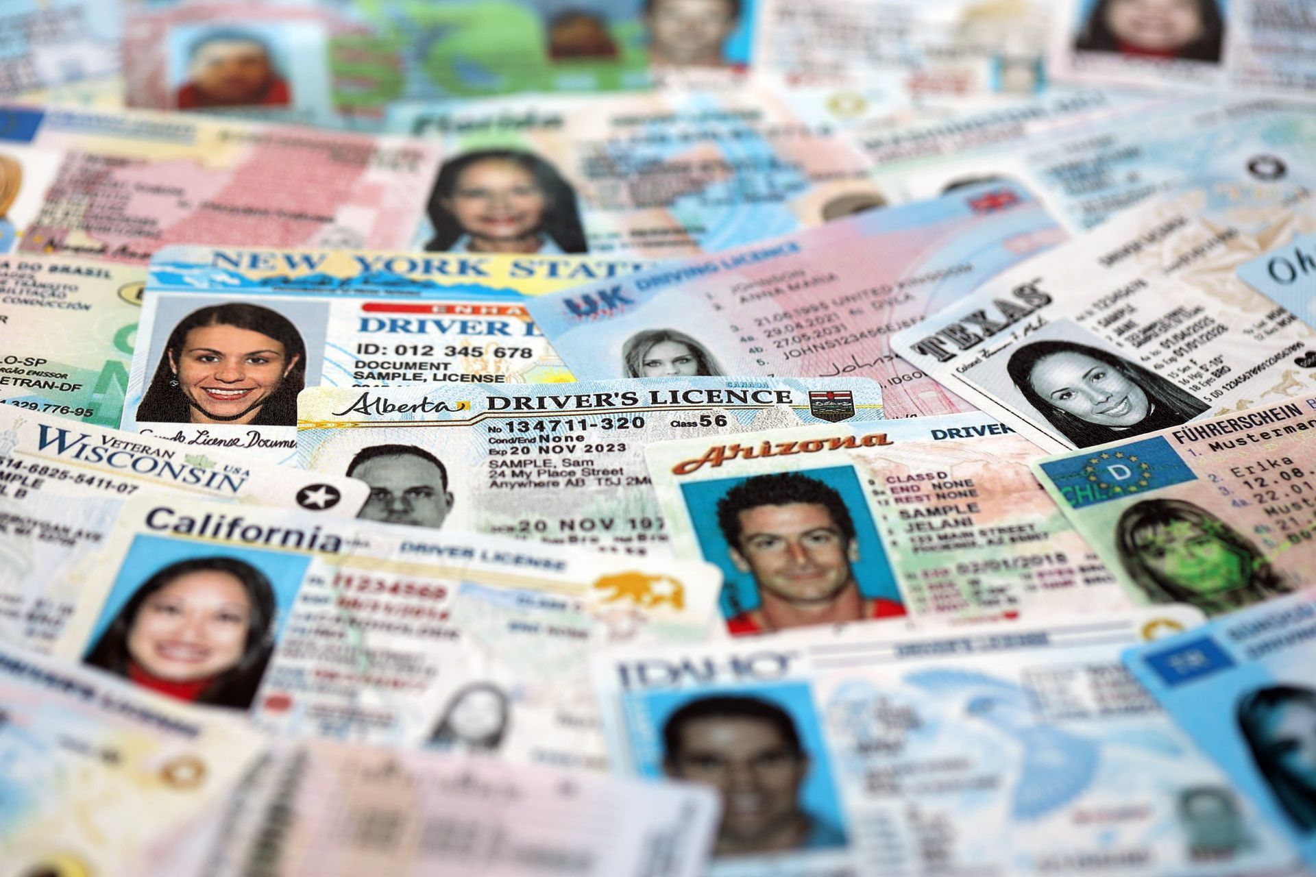 Assorted ID cards and driver’s licenses spread out in a pile, showing many faces and state names