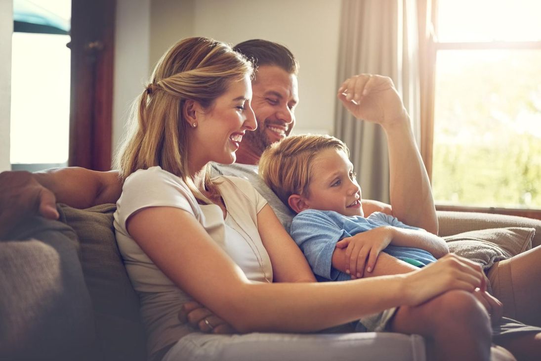 Smiling family relaxing on a couch, with sunlight streaming through the window