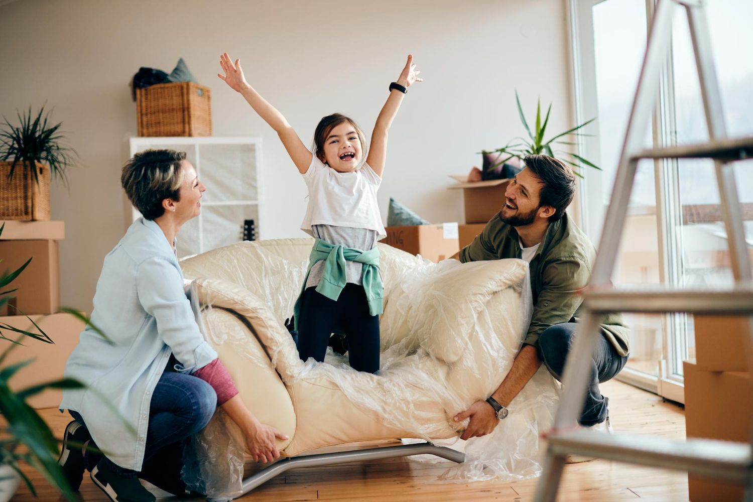 A family is moving into a new home and a little girl is sitting on a couch.