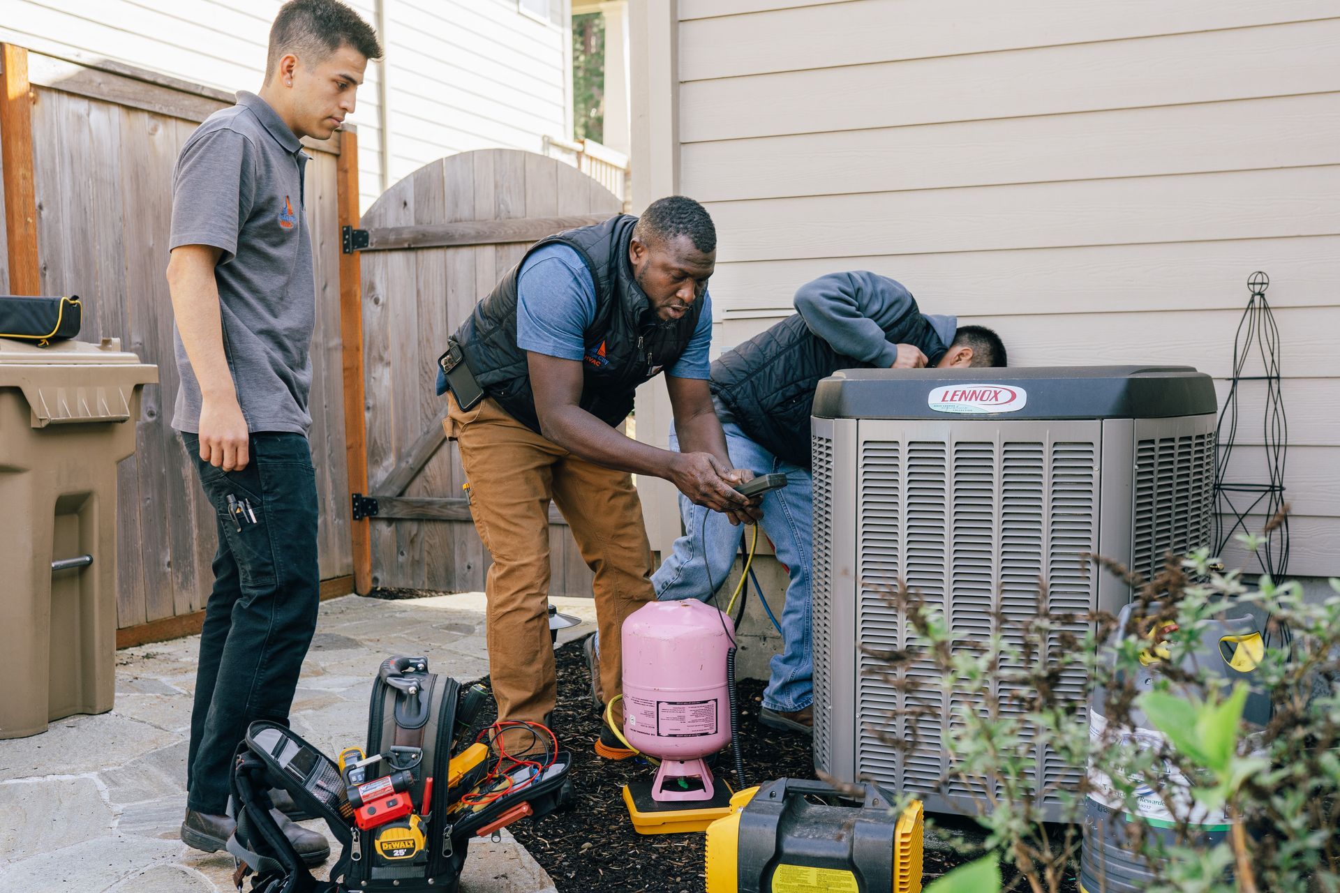 A group of men are working on an air conditioner outside of a house.