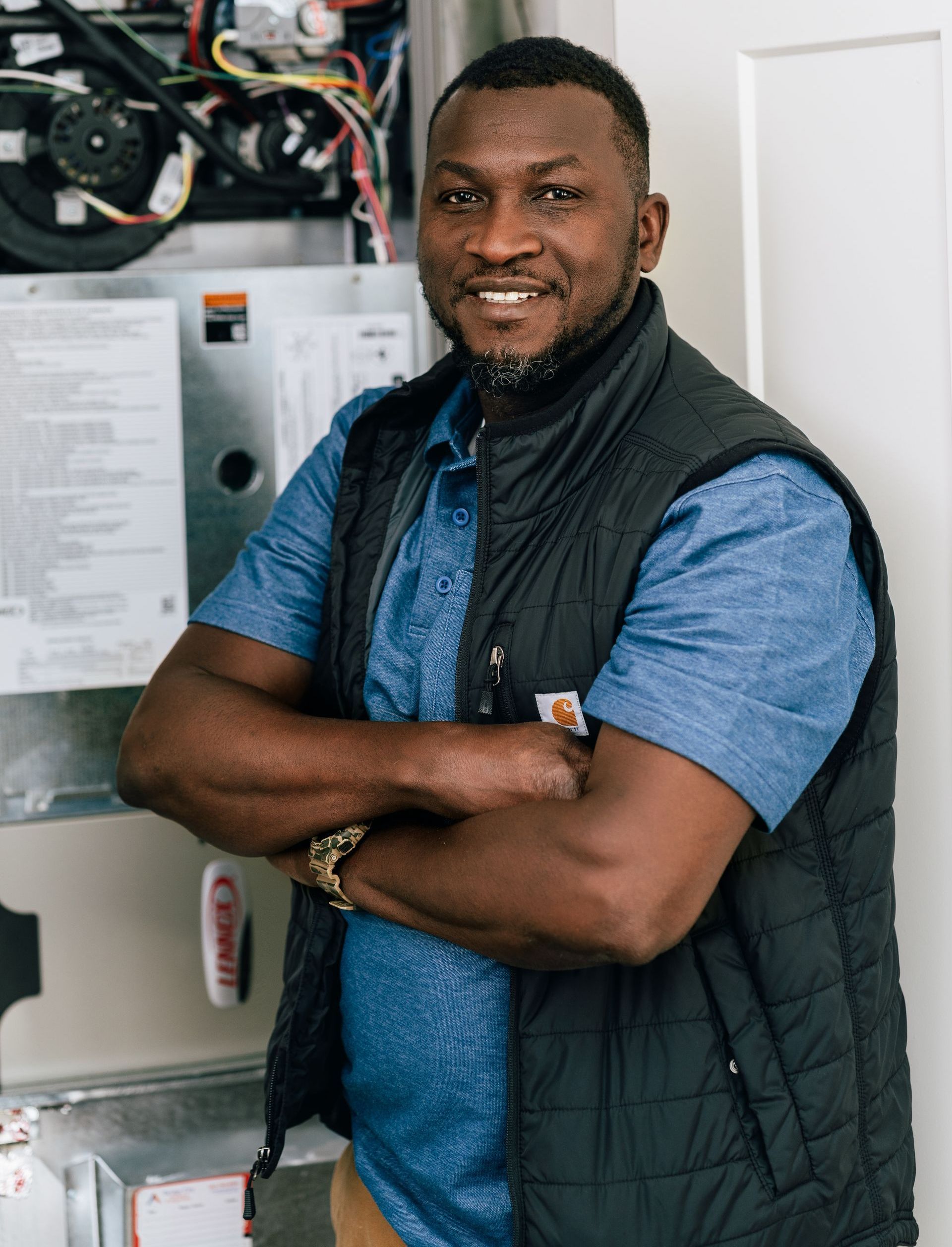 A man is standing in front of an air conditioner with his arms crossed.