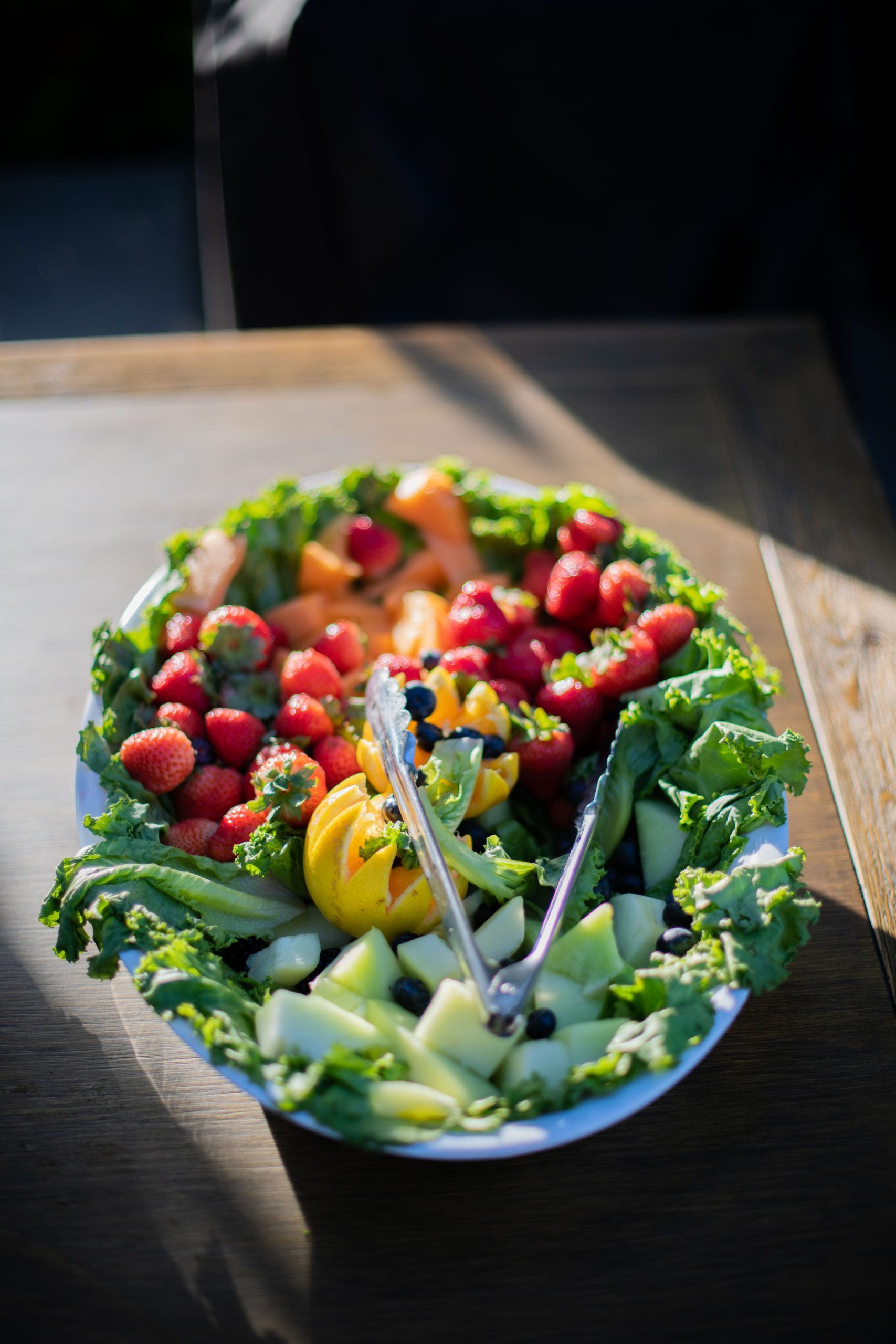 Fruit platter with strawberries, melon, and lettuce on a white plate.