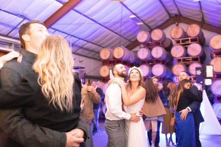 Wedding reception: dancing couples in a barrel room with purple lighting.