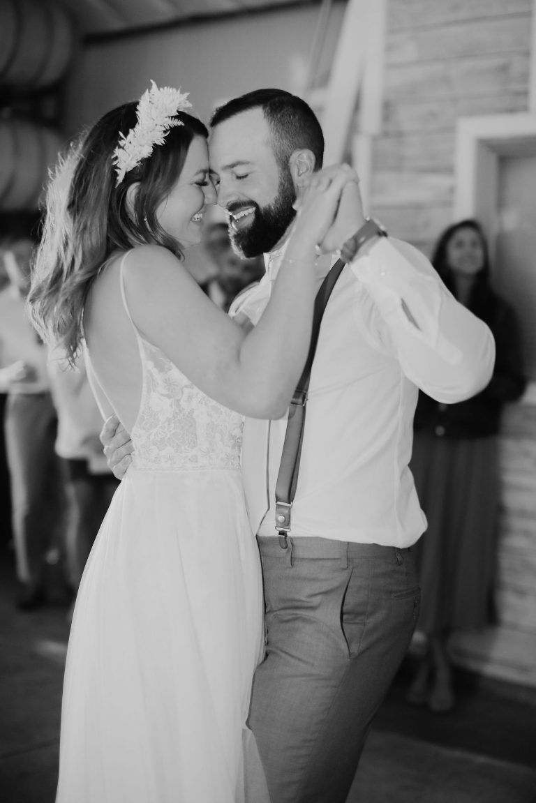 Bride and groom dance at reception. Woman in white dress, flower crown, man in suspenders, hugging.