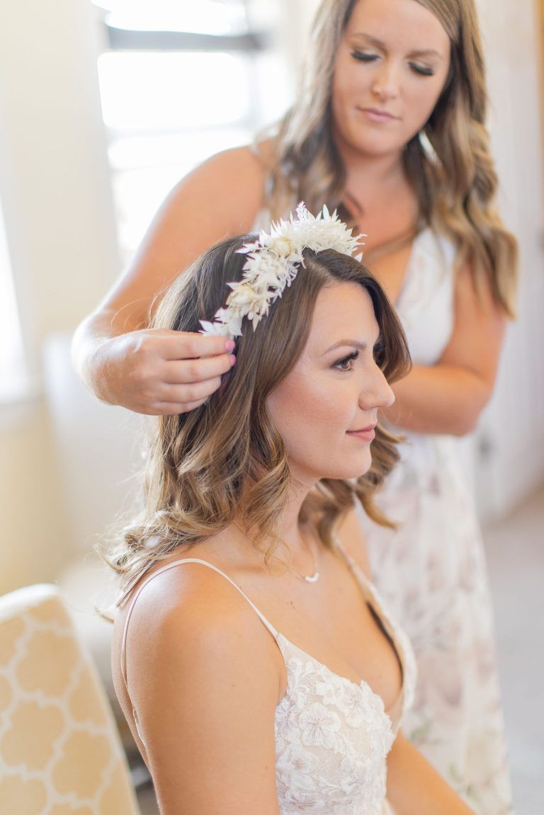 Woman in wedding dress having floral crown adjusted by another woman.