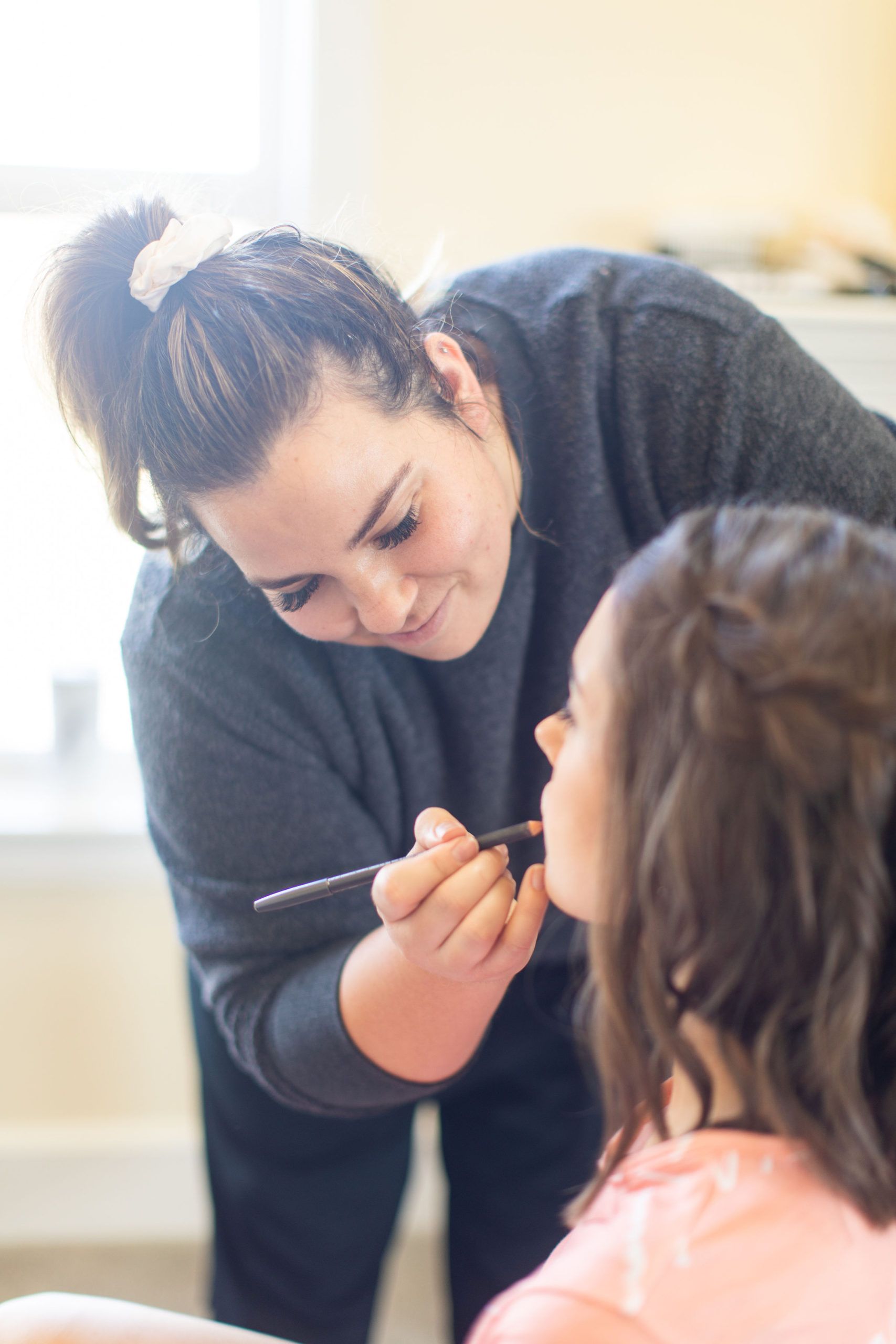 Woman applying lipstick to another woman's lips, indoor setting.