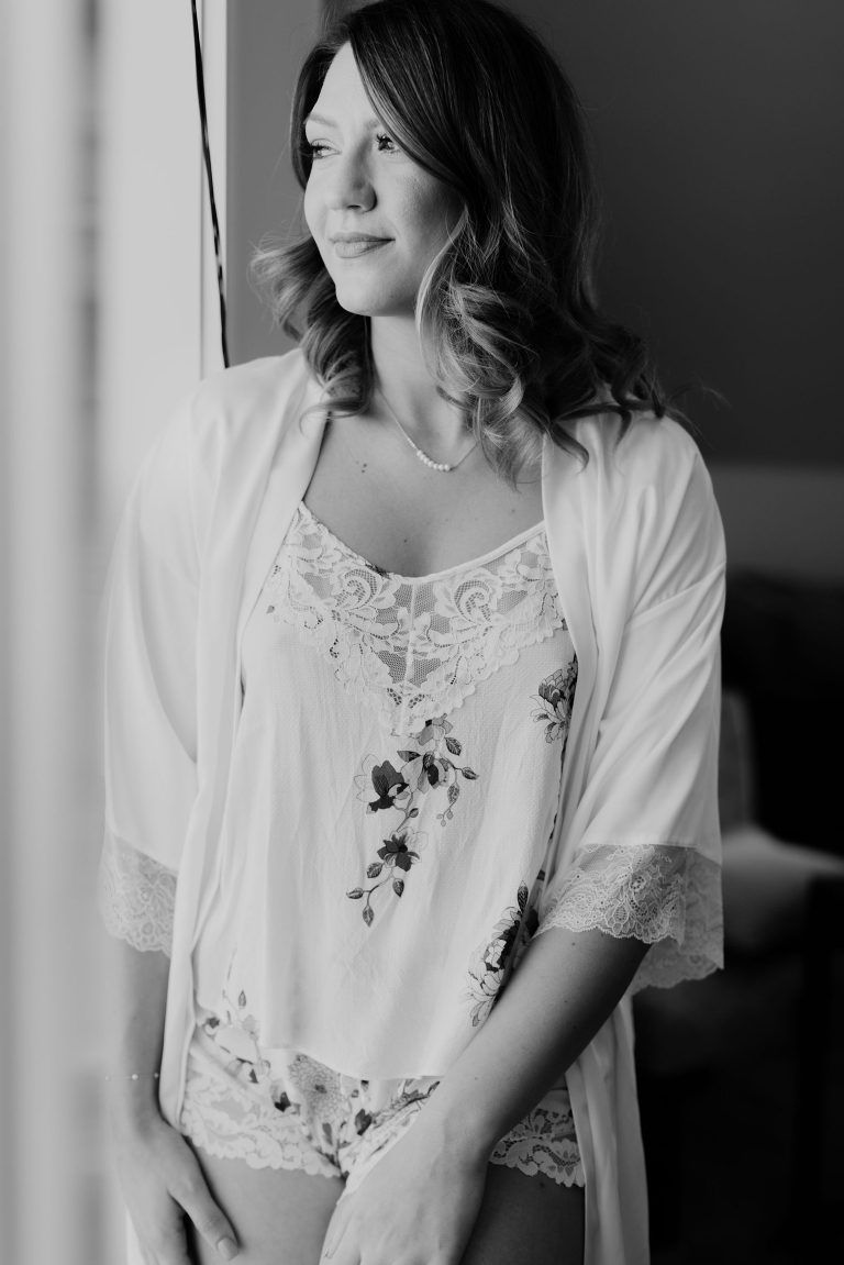 Woman in lingerie and robe, looking out a window. Black and white photo.