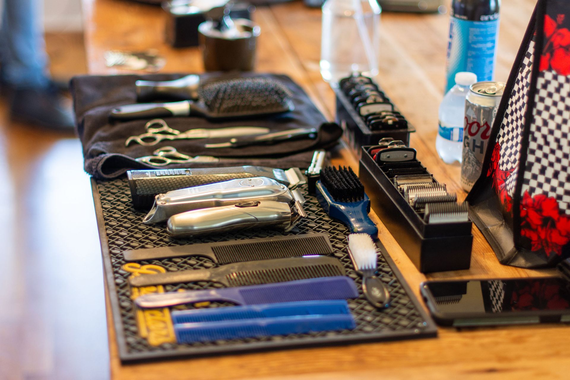Hairdresser's tools arranged on a wooden table: scissors, combs, clippers, brushes, and a cell phone.