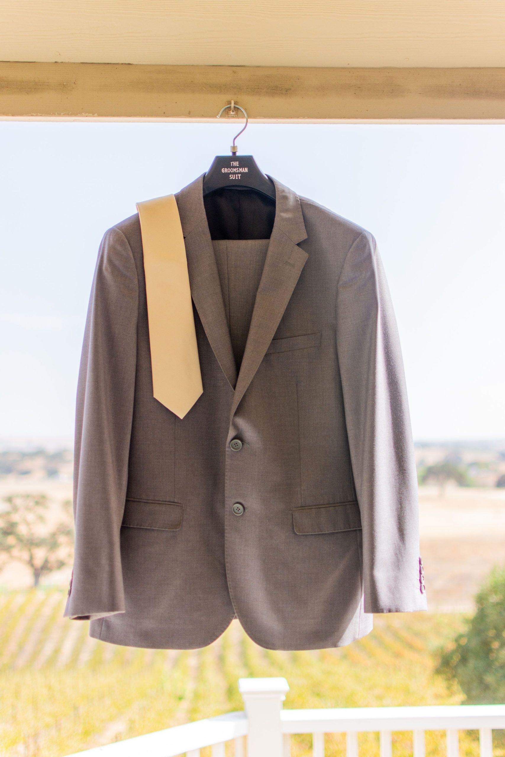 Gray suit jacket and pants with a yellow tie hanging on a hanger outdoors.