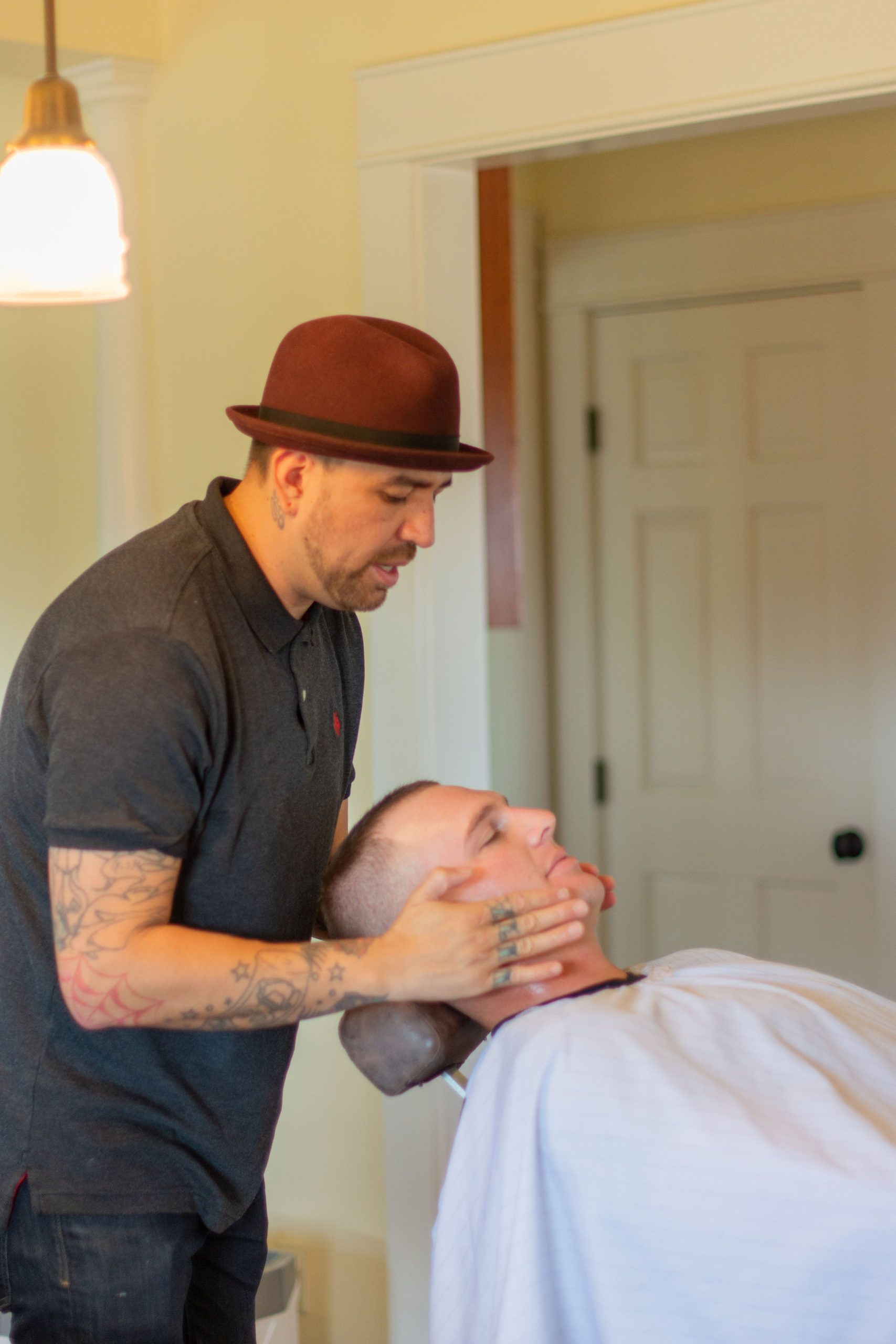 Barber with a maroon bowler hat, preparing a client for shaving in a shop setting.