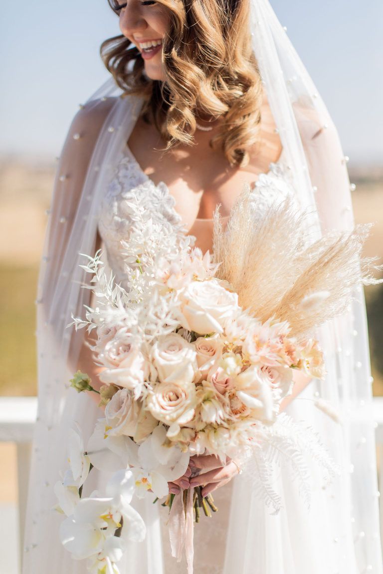 Bride holding a bouquet of cream and pink roses, wearing a veil.
