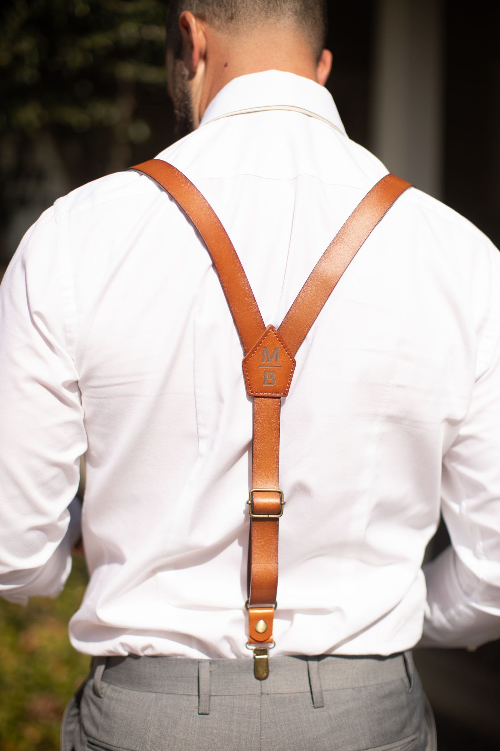 Man wearing brown leather suspenders over a white dress shirt and gray trousers.