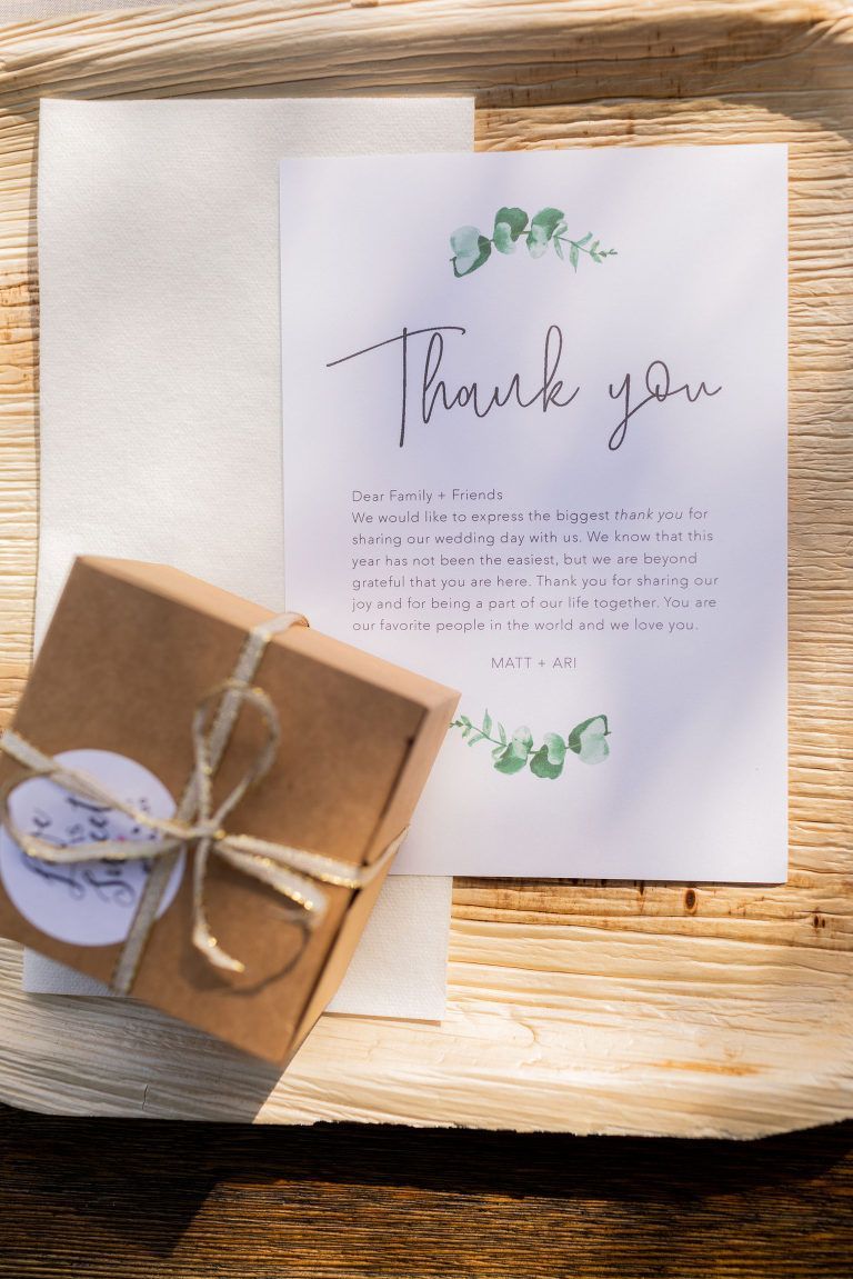 Thank you card with green eucalyptus accents, a small gift box, and an envelope on a wooden tray.
