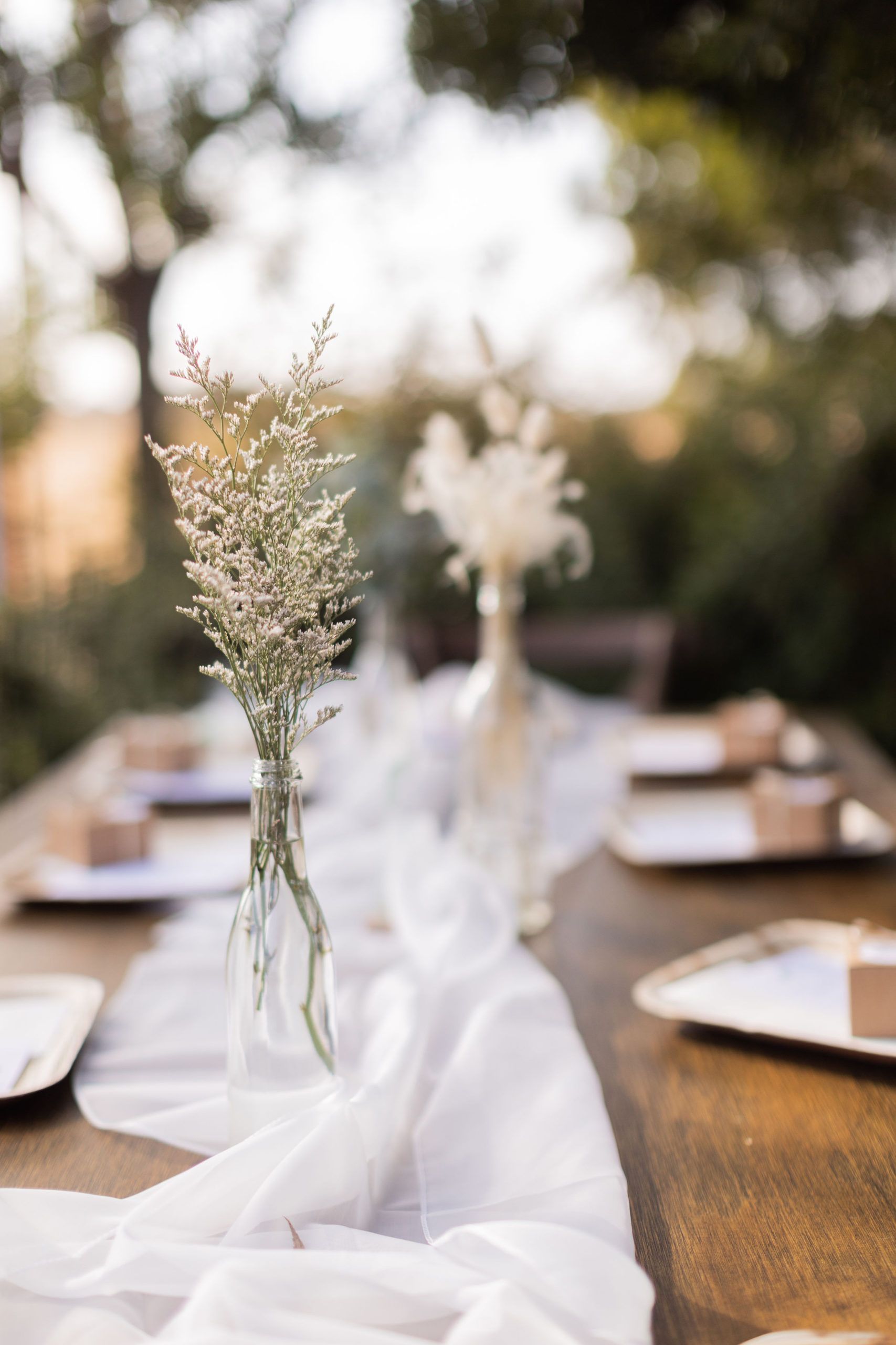 Table setting with flowers in glass bottles, a white table runner, and place settings.