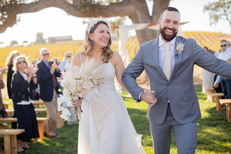 Newlyweds walking down aisle, smiling. Wedding ceremony outdoors.