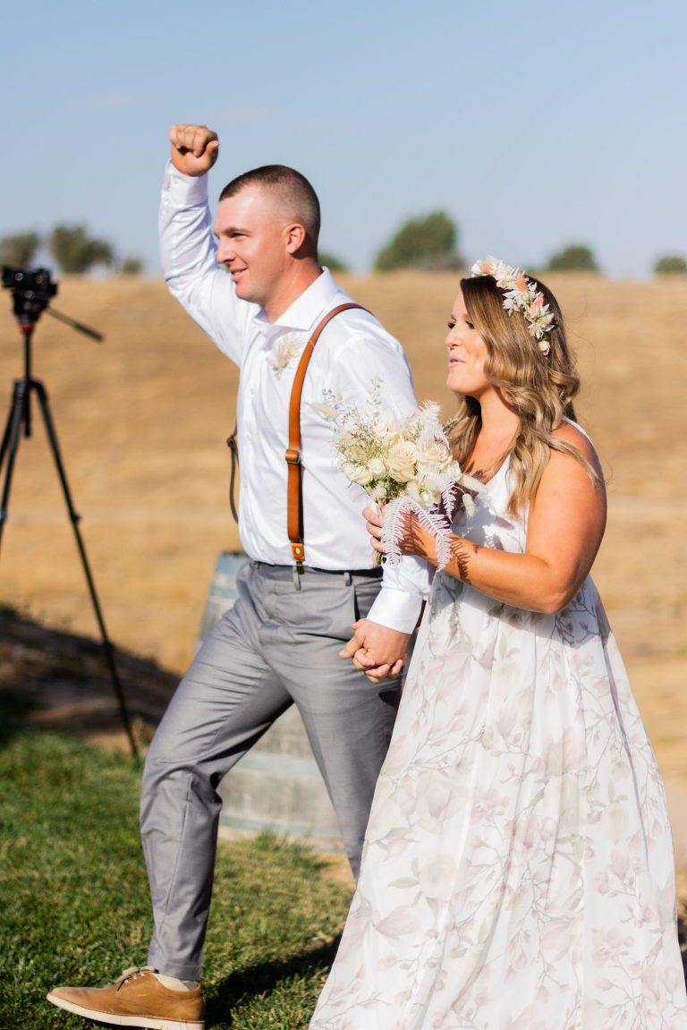 Newly married couple celebrating, man raises fist, woman smiles. Outdoor wedding.
