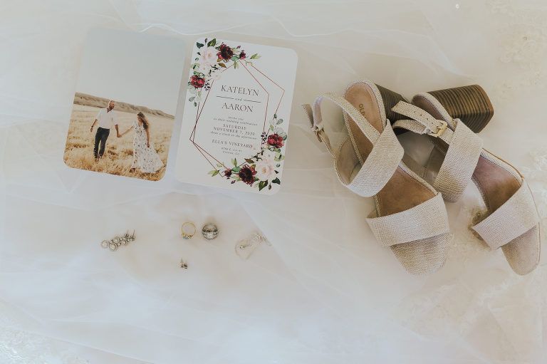 Wedding details: invitation, bride's shoes, earrings, and photo on white surface.