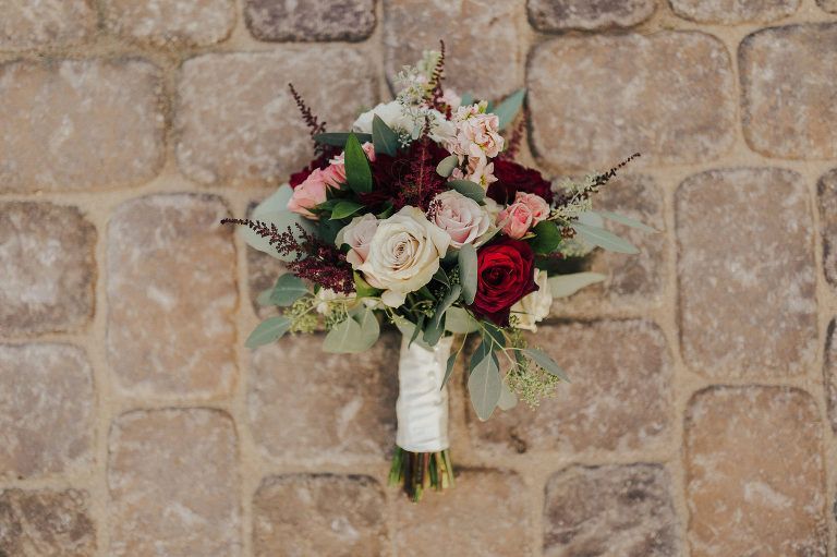 Wedding bouquet with roses and greenery against a stone wall.