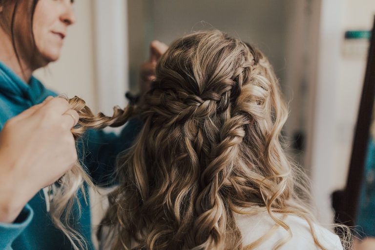 Woman getting her hair styled: blonde curls, braids, indoor, hands working.