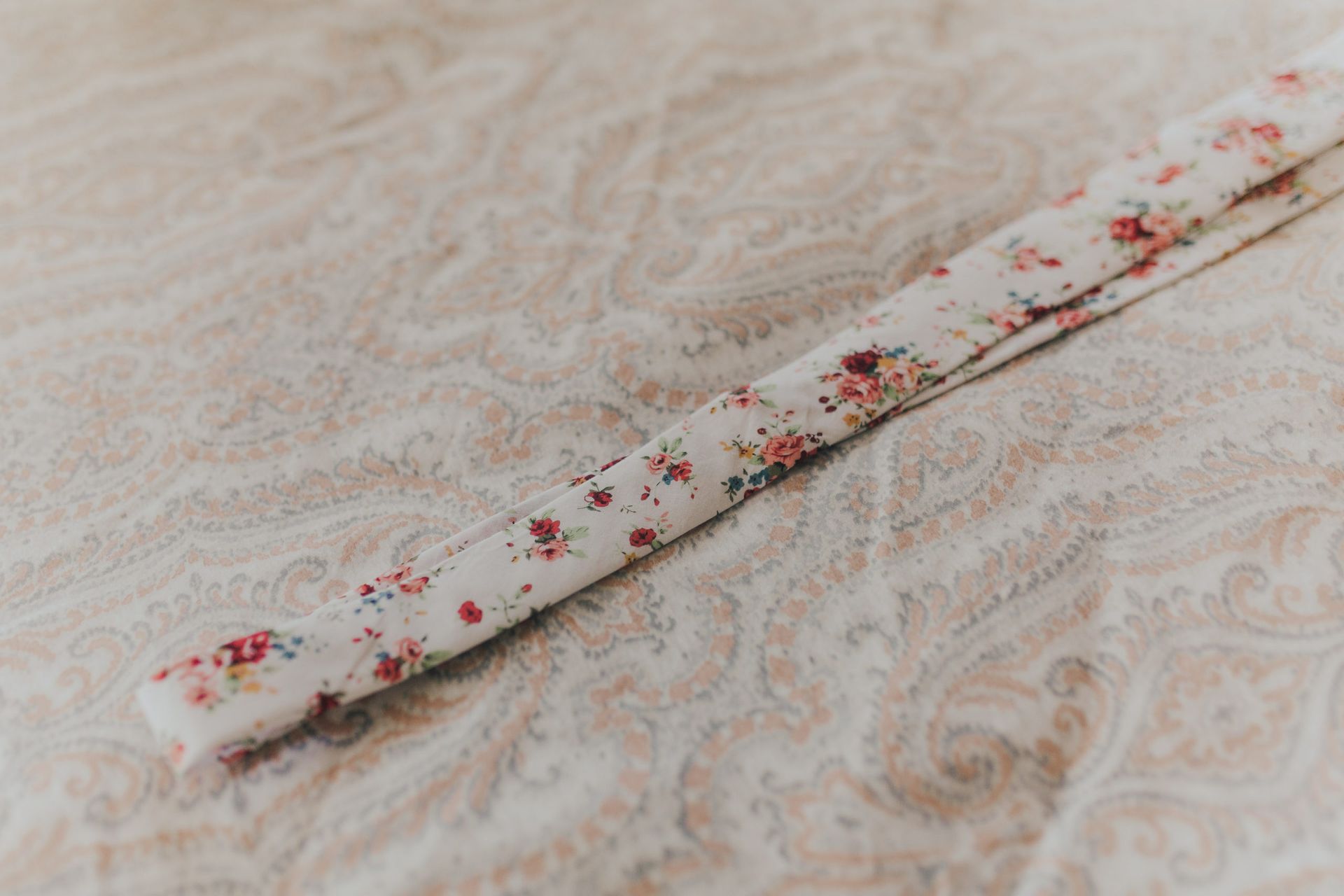 White floral fabric strip on paisley patterned beige surface.