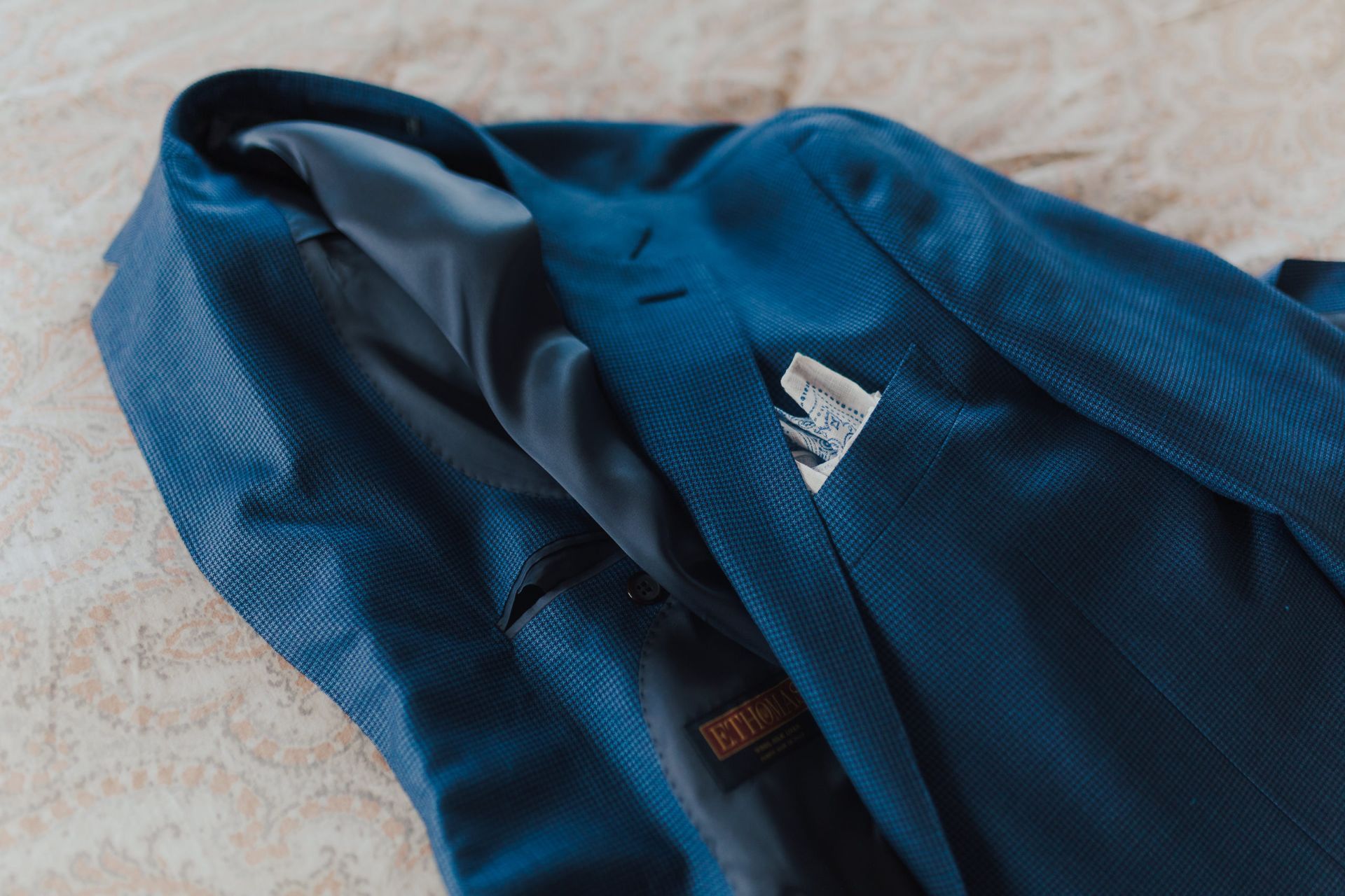 Blue suit jacket, with a pocket square, lying on a light-colored surface.
