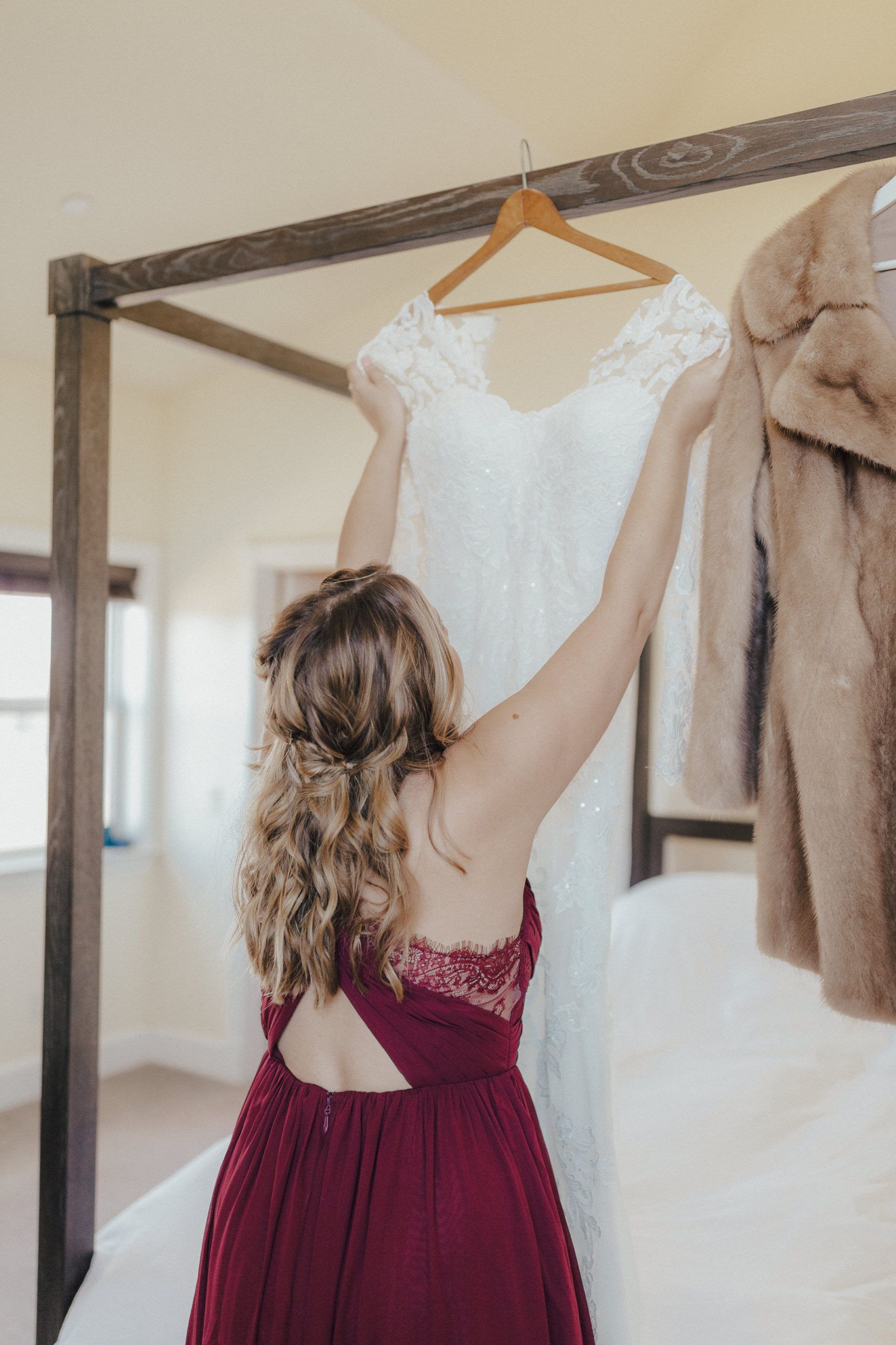Woman in burgundy dress hanging a white wedding gown on a wooden hanger.