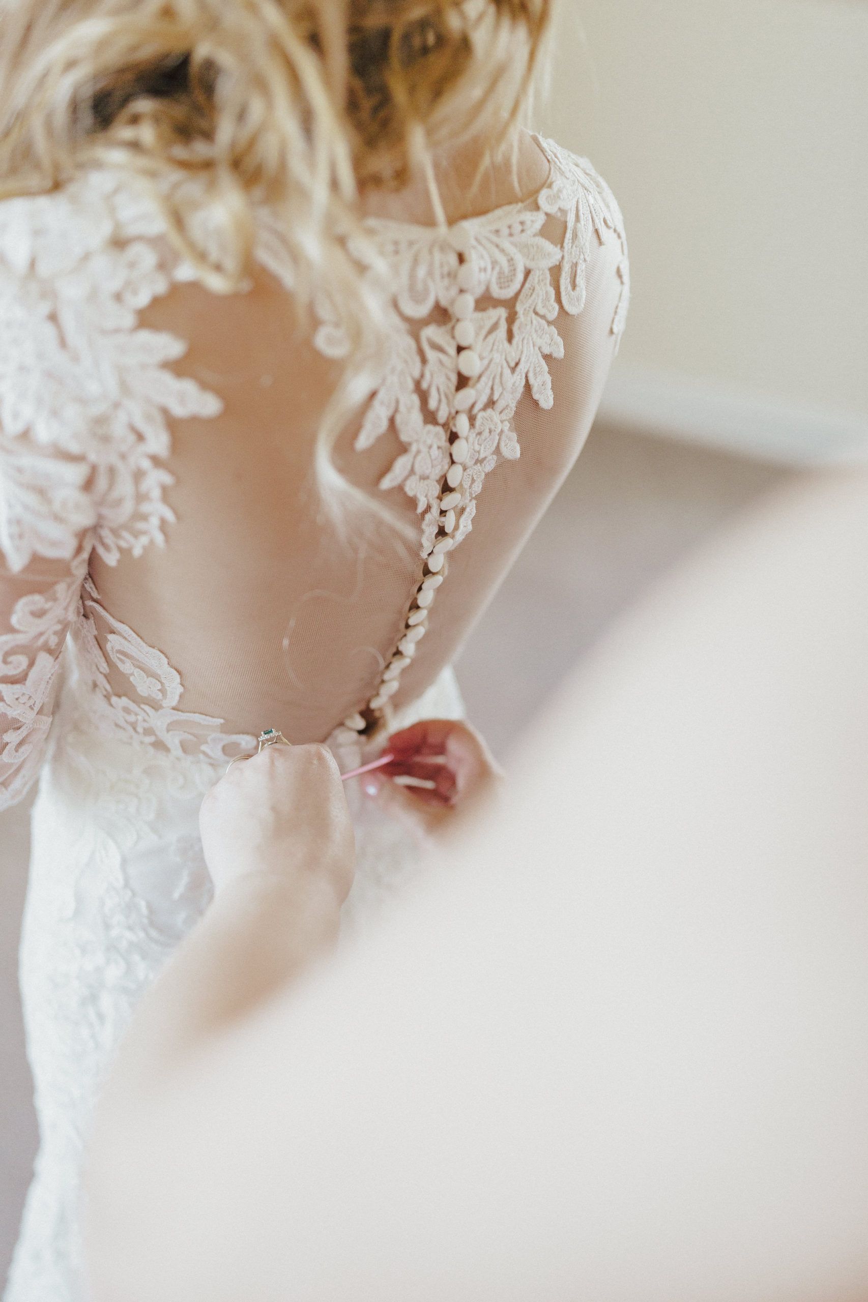 Bride in lace wedding dress, back view, having buttons fastened.