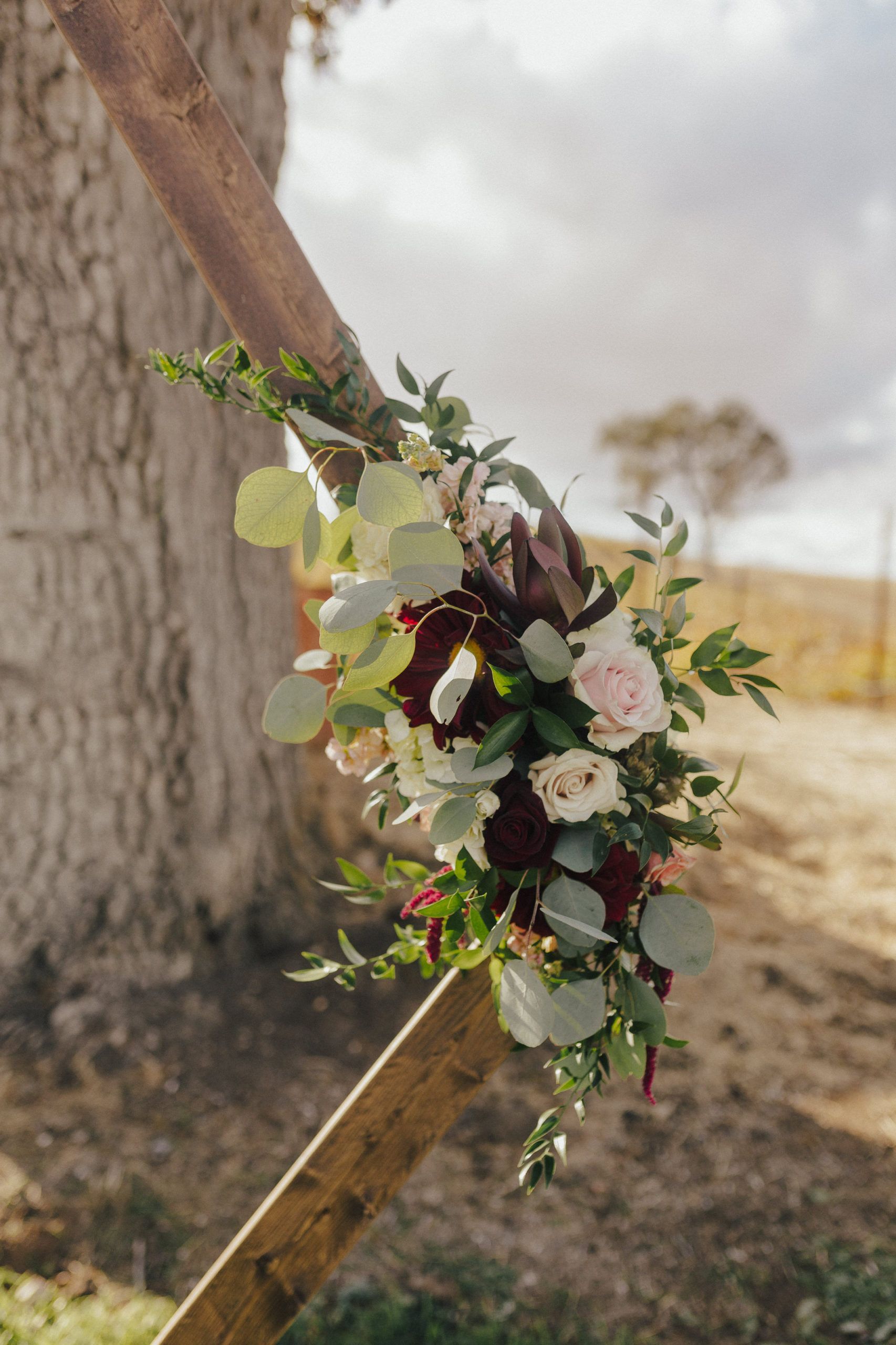 Floral arrangement of red, white, and pink flowers and greenery attached to a wooden structure, outdoors.