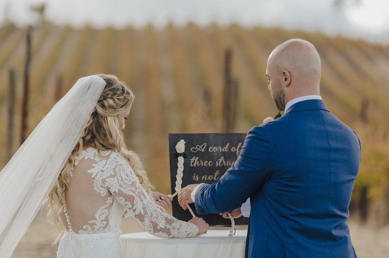 Bride and groom braiding cords at wedding ceremony in vineyard.
