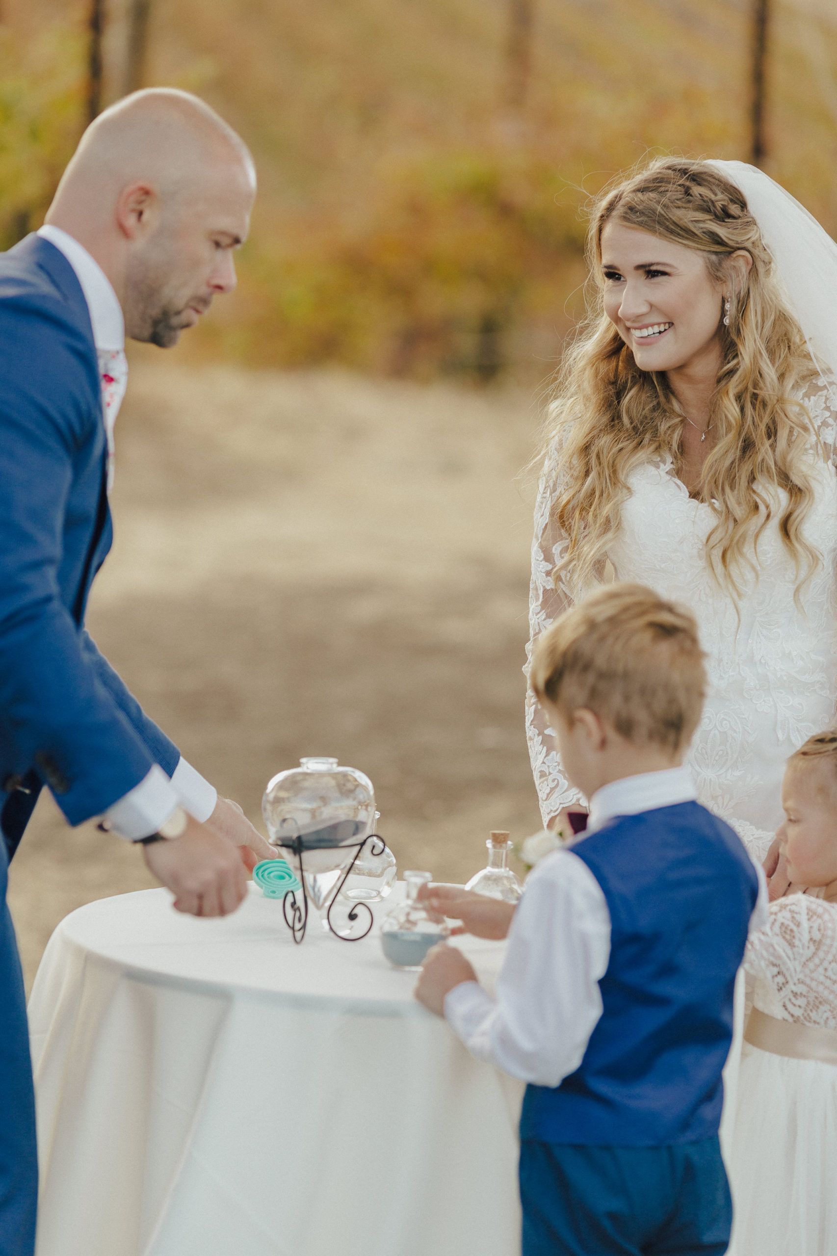 Groom, bride, and children at a wedding ceremony, near a table with cookies, in an outdoor setting.