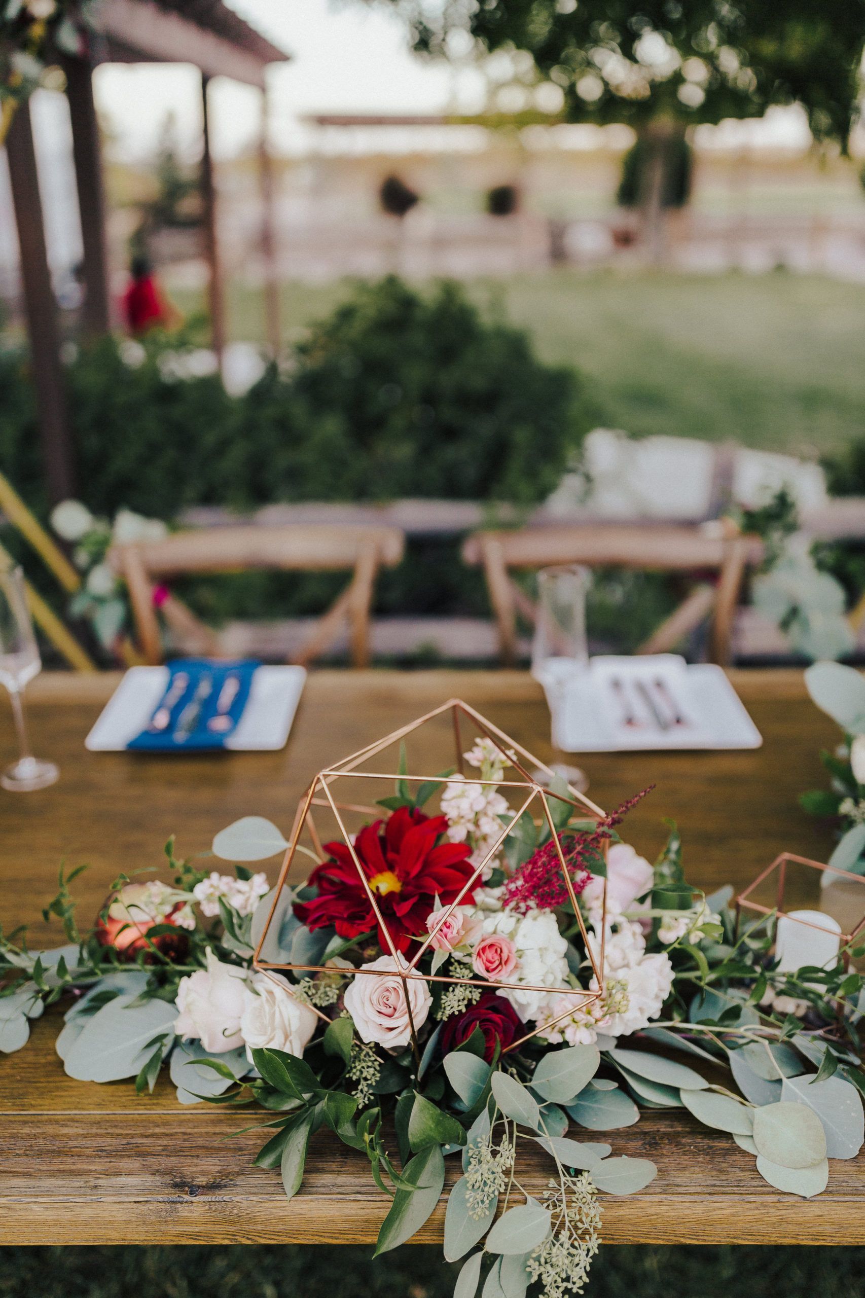 Wedding reception table with floral centerpiece and place settings, outdoors.