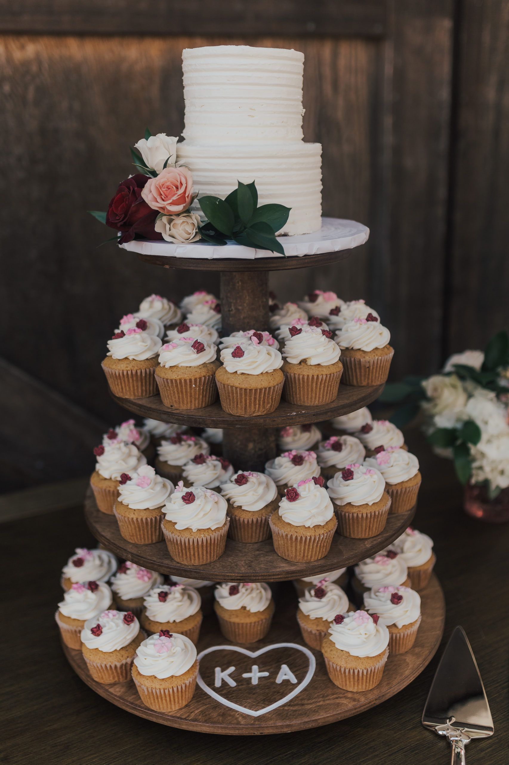 Wedding cake with cupcakes on a tiered stand. Top tier: white cake with flowers. Lower tiers: cupcakes with frosting and berries.