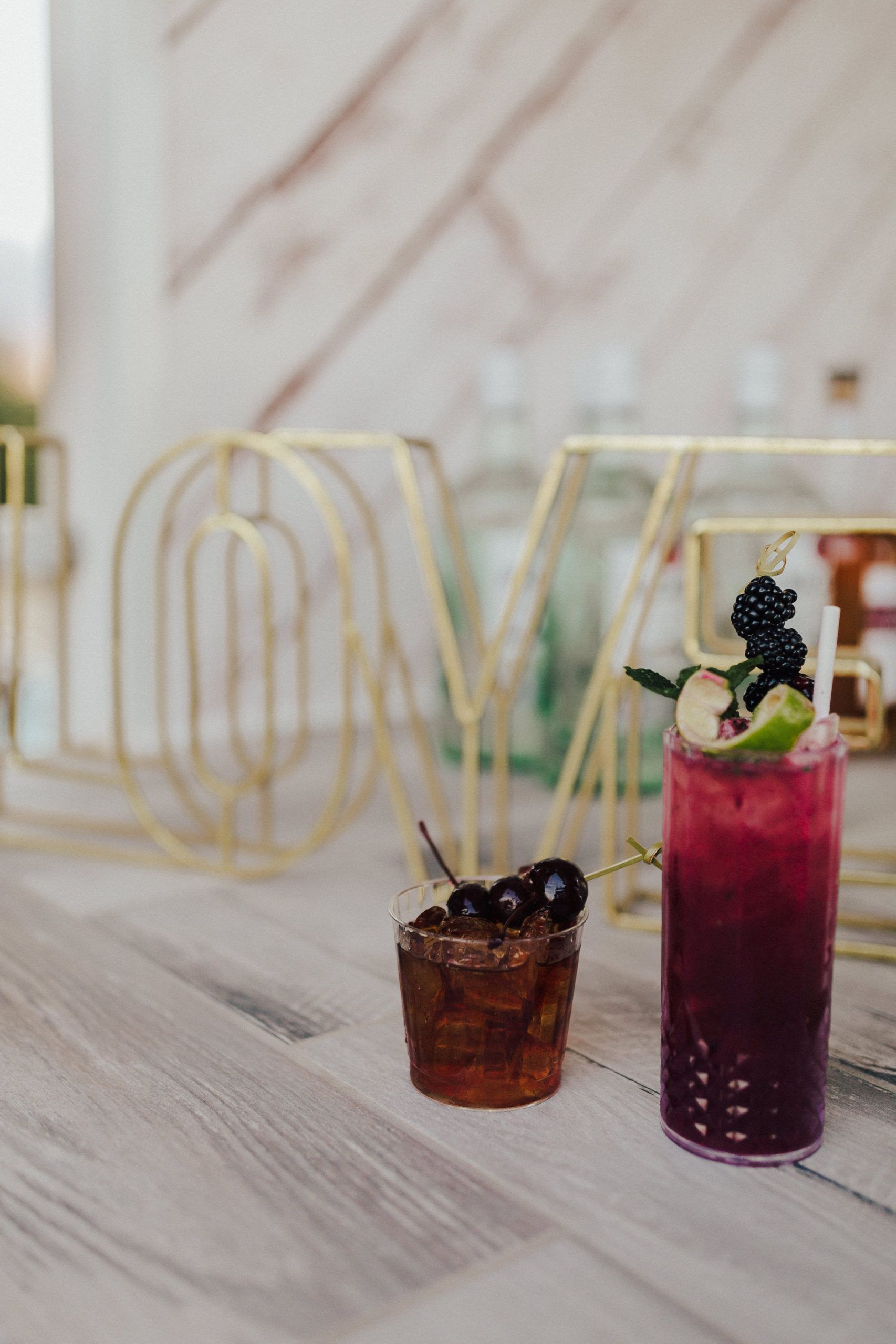 Two colorful cocktails on a light wooden surface with a gold 